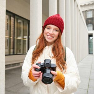 Smiling redhead girl photographer, taking pictures in city, makes photos outdoors on professional